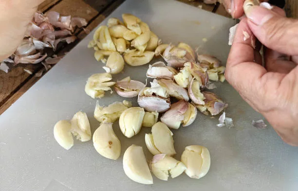 Woman peeling garlic on the cutting board for cooking.