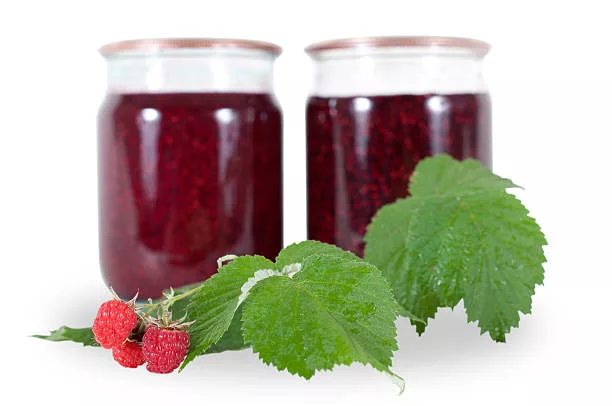 raspberries and two cans of raspberry jam on a white background